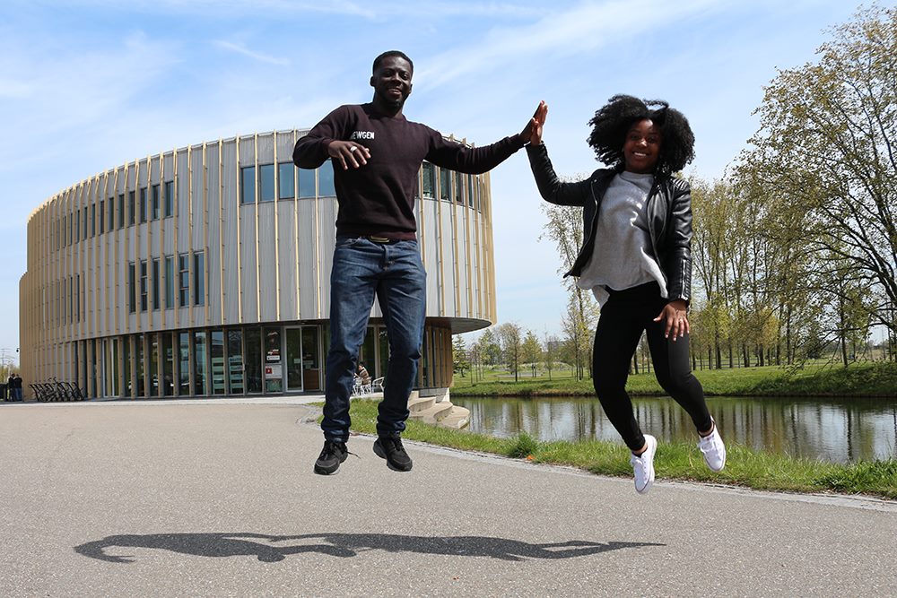 Twee vrolijke jonge mensen springen in de lucht voor een modern gebouw
